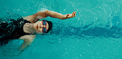 A woman wearing swim goggles swimming on her back