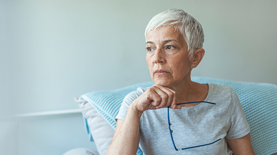 A woman leaning against a pillow and holding her glasses and looking to the side.