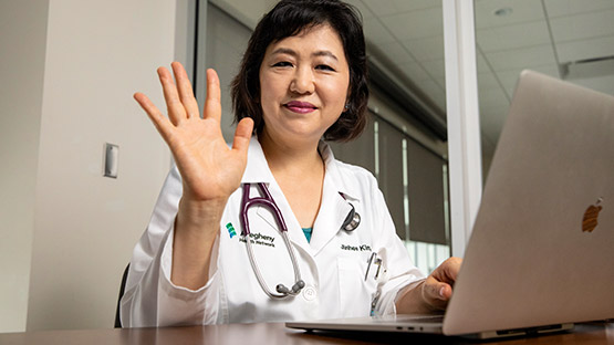 A doctor waving to a patient on their laptop during a video visit.