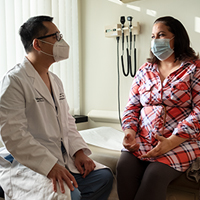 An AHN physician wearing a mask sitting next to a patient and talking about her diagnosis.