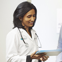 A doctor standing next to another physician while looking at her tablet.