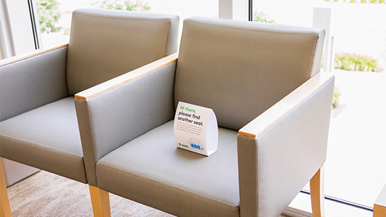 A small social distancing sign that has been placed on a chair in the waiting room.