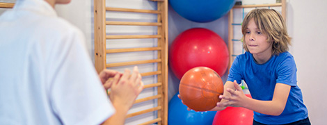 A young boy throwing a medicine ball during physical therapy.